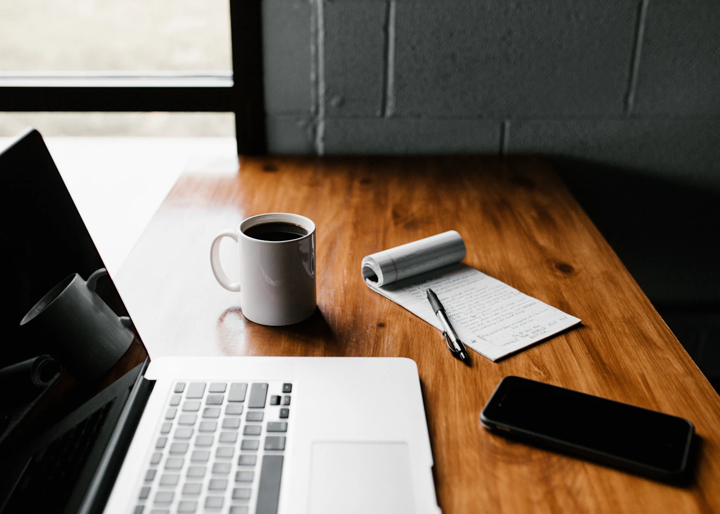 Laptop, handwritten notes, phone, and coffee on a wooden table
