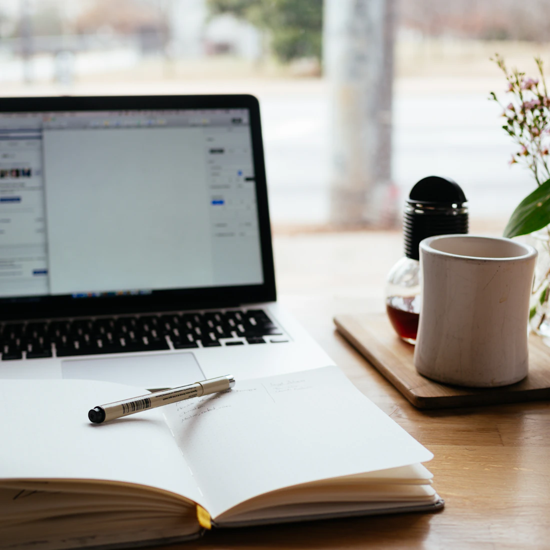 Laptop, open notebook, and coffee beside a sunlit window