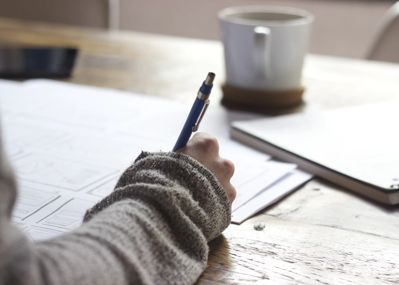 Person writing notes beside a laptop and coffee